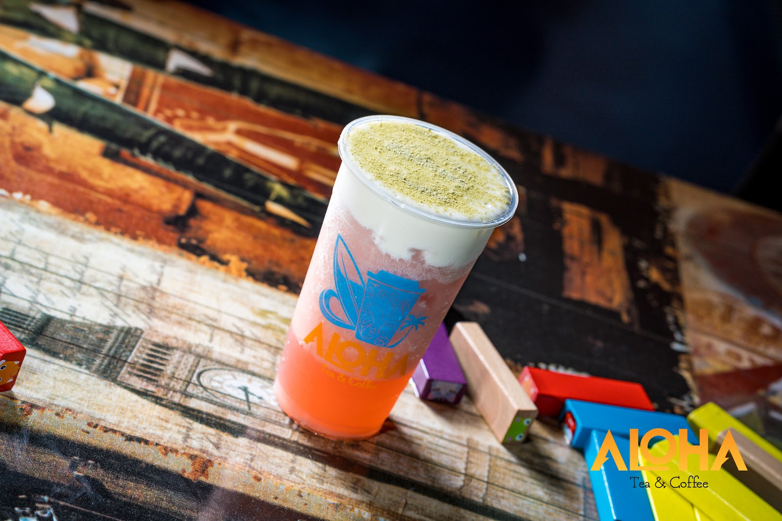 A layered strawberry drink with matcha cream in an Aloha Tea Coffee cup